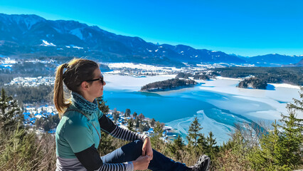 Hiker woman on top of Taborhoehe viewing platform in Carinthia, Austria, Europe. Surrounded by snow capped Karawanks mountains. Frozen Lake Faak. Alpine Landscape in frosty winter in Austrian Alps