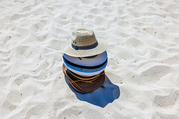 Stack of summer hats sold by local vendors on Mexican beach, resting on white sand under bright...