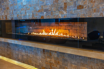 Modern linear gas fireplace with vibrant flames set against textured stone wall in cozy interior...