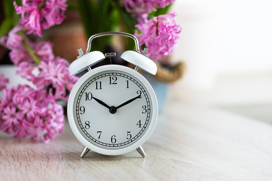 Spring change, Daylight Saving Time concept. White alarm clock and hyacinth flowers on the wooden table. Springtime home gardening, hobby, leisure. Copy space for text