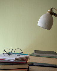 glasses on a stack of books on a desk with a reading lamp