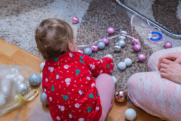 Fototapeta premium The little child playing with Christmas balls, with mother in nearby. Christmas holiday spirit 