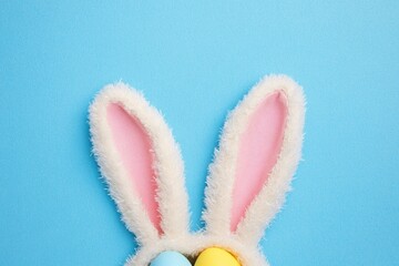 Obraz premium Festive Easter Celebration. Top View of Colorful Bunny Ears and Bright Eggs on Soft Blue Background