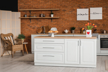 Interior of modern kitchen with bouquet of tulip flowers and greeting card on wooden counter