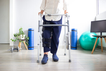 Lower-body view of a senior walking with a walker and wearing a leg immobilizer on the right leg....
