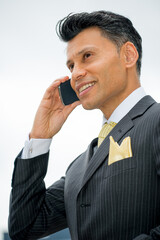 Smiling smartly dressed Asian / Middle eastern businessman holding a mobile phone to his ear, in an outdoor city location.