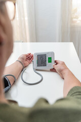 Senior woman checking blood pressure at home using digital sphygmomanometer