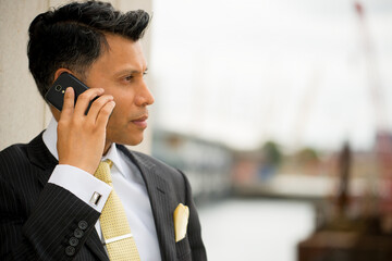 Serious, smartly dressed Asian / Middle eastern businessman holding a mobile phone to his ear, in an outdoor city location.