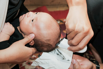 Southeast parents shaving hair of her baby boy with electric hair clipper after Aqiqah ceremony,...