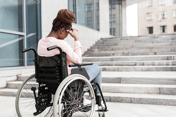 Unhappy young black woman suffering from lack of wheelchair friendly facilities, cannot get home without ramp, copy space. Inaccessible city environment for people with special needs concept