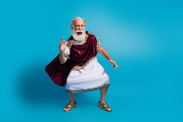 Photo of crazy cheerful man antique greek king dancing in toga mantle clothes isolated on blue...
