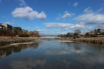 Obraz premium 鴨川の穏やかな冬景色 - 青空とリフレクションが広がる美しい風景 / Tranquil Winter Scenery of Kamogawa River - Stunning Blue Sky and Reflections