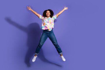 Joyful young woman with curly hair jumps enthusiastically against a vibrant purple background