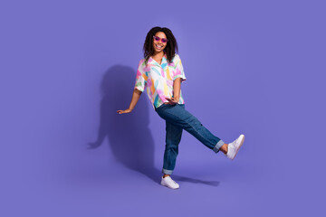 A young woman with vibrant energy stands in a joyful pose, set against a purple backdrop wearing fashionable casual clothing