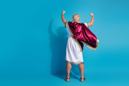 Full length photo of old man back view raise fists celebrate winner dressed greek god emperor actor costume isolated on blue background