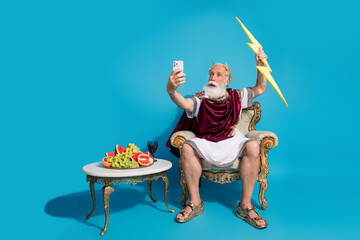 Full size photo of ancient myth character god hold lightning make selfie phone isolated on blue color background © deagreez