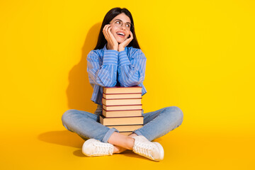 Young smiling woman seated with books against a vibrant yellow background