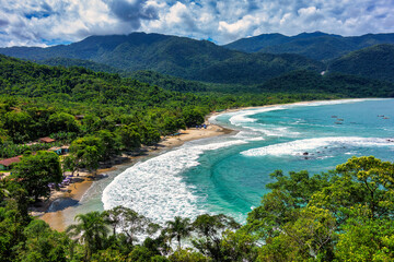 Castelhanos Beach in Ilhabela, Sao Paulo, Brazil. View from the lookout point of the heart-shaped Castelhanos Beach, surrounded by Atlantic Forest, on a sunny day with blue sky and clouds