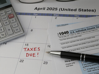 A 2025 calendar noting the April 15 USA Internal Revenue Service IRS income filing deadline for year 2024 taxes is shown up close, with a calculator, ink pen, and glasses in the frame.