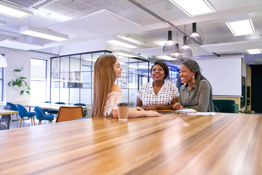 Group of three young mixed race students practicing teamwork together in large open coworking space