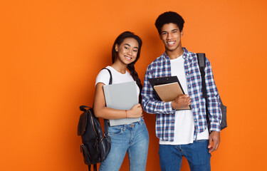 Happy students wearing backpacks and holding exercise books, orange background