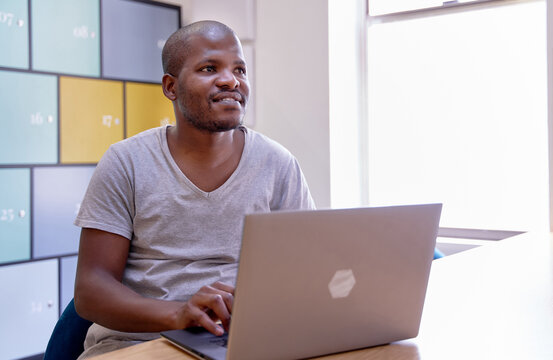 Handsome bald African American man thinking casually at wooden table in bright room