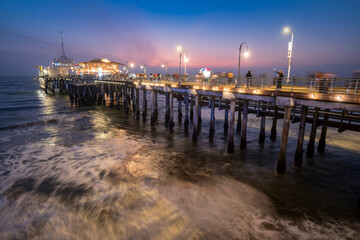 Santa Monica pier at dusk with people walking about and blurry ocean waves
