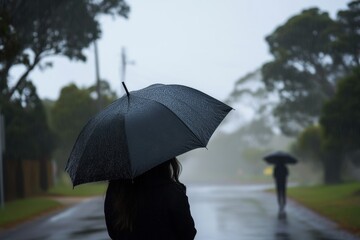 A person walks with an umbrella on a rainy street as another figure appears in the distance. Generative AI