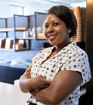 Portrait of natural smiling black professional businesswoman with arms crossed in modern coffee shop