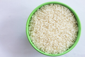 Raw rice is contained in a small green bowl, isolated on a white background