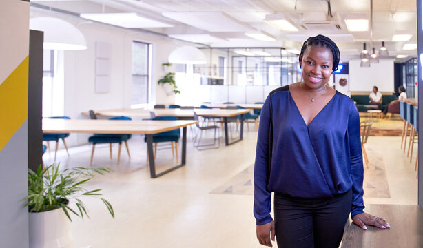 Positive, charming, confident natural African American woman standing in trendy office smiling wearing fashionable clothing