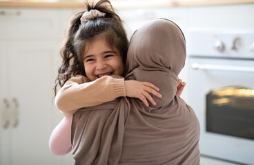 Cute Little Girl Hugging Her Muslim Mom In Headscarf And Smiling, Loving Family Bonding With Each...