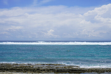 Vertical capture of crystal-clear ocean waters meeting the rugged shoreline under a bright, sunny sky.