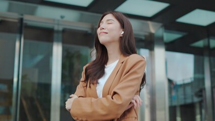 Confident Young Asian Female Enjoying Music with Wireless Earbuds, Standing Cheerfully in a Bright sunnyday Urban Setting. Cheerfully in a Bright Urban Setting