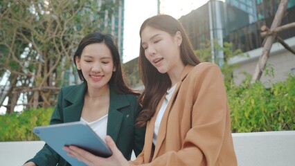 Asian Businesswomen Collaborating Outdoors: Sharing Ideas and Plans with a Tablet in an Urban Greenery Setting. Professional Asian Women Discussing Digital Marketing. Remote work online outdoors