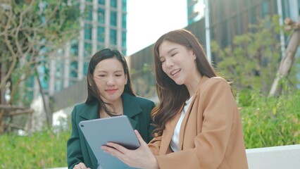 Asian Businesswomen Collaborating Outdoors: Sharing Ideas and Plans with a Tablet in an Urban Greenery Setting. Professional Asian Women Discussing Digital Marketing. Remote work online outdoors