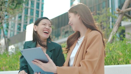 Asian Businesswomen Collaborating Outdoors: Sharing Ideas and Plans with a Tablet in an Urban Greenery Setting. Professional Asian Women Discussing Digital Marketing. Remote work online outdoors