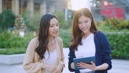 Asian Businesswomen Collaborating Outdoors: Sharing Ideas and Plans with a Tablet in an Urban Greenery Setting. Professional Asian Women Discussing Digital Marketing. Remote work online outdoors