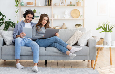 Young family spending weekend at home, using laptop and digital tablet, empty space