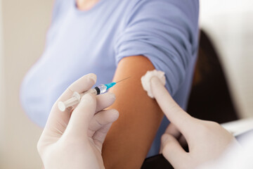 Closeup of doctor hands in protective gloves injecting vaccination in arm of unrecognizable female patient in clinic, cropped. Vaccination against COVID-19, healthcare and medical concept