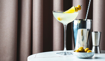 Mexican martini, alcoholic cocktail drink with tequila, liqueur, lime juice and green olives. Marble table with fabric curtain background