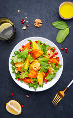 Winter vegan  persimmon salad with pomegranate, walnuts, oranges and lettuce, black background, top view