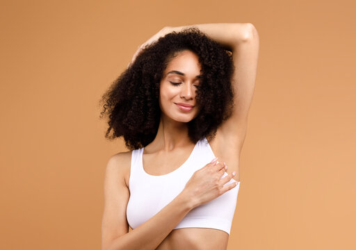 Hair removal concept. Happy latin lady demonstrating her armpit with smooth skin and smiling, posing in white underwear over brown background, copy space