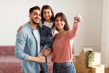 Portrait Of Happy Young Family Showing Key, Cheerful Parents Hugging Little Kid, Holding Daughter...