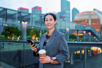Confident Businesswoman with Smartphone and Coffee in a Modern Urban Setting