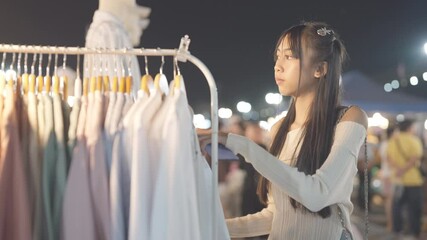 A woman is shopping for clothes in a store. She is looking at a rack of clothes and holding a cell phone