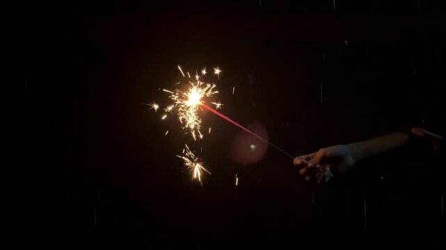 Asian Indonesian child's hand holds sparkling fireworks at night, simple joyful kids celebration.