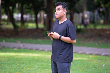 Asian runner with smartphone while running in the park. Sports athlete doing exercise for heart health, physical fitness and marathon training
