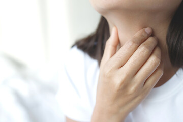 sore throat pain. Closeup of young woman sick holding her inflamed throat using hands to touch the ill neck in blue shirt on gray background. Medical and healthcare concept.