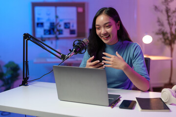 Happy young content creator recording a podcast at home, using a laptop and professional...